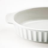 White, oval stoneware baking dish with side handles and ribbed design.