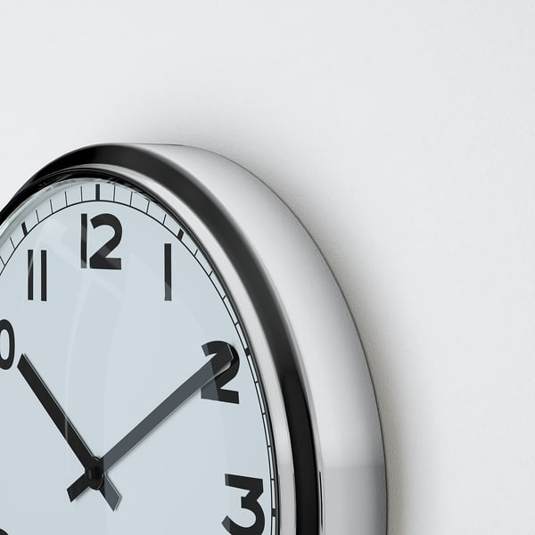 Close-up of round wall clock with black hands and numbers, white face, and silver frame. Time shown is 10:10.