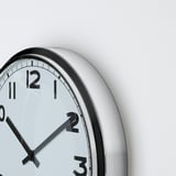 Close-up of round wall clock with black hands and numbers, white face, and silver frame. Time shown is 10:10.