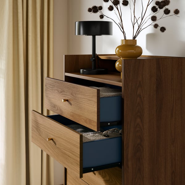 Wooden chest with blue drawers, open drawer, black lamp, yellow vase, beige curtains.