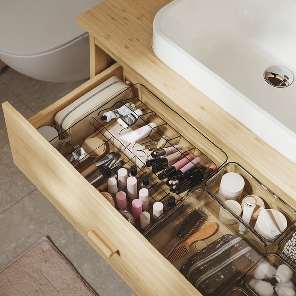 Wooden bathroom drawer with clear organizers holding makeup and toiletries.