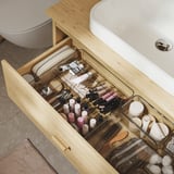 Wooden bathroom drawer with clear organizers holding makeup and toiletries.