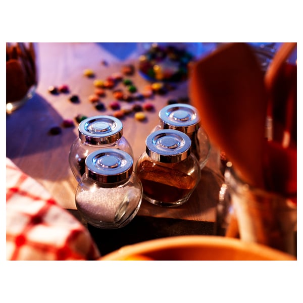 Four clear glass jars with metallic lids on a table by colorful candies.