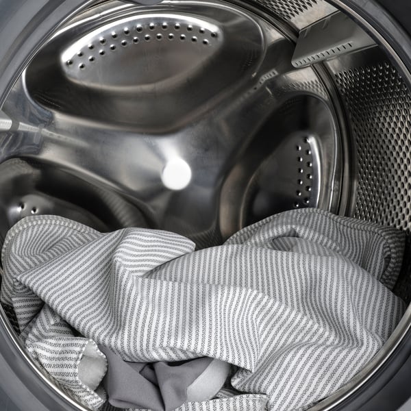 Striped bedsheet inside metal drum washer, highlighting RAMNEFJÄLLs machine washable feature.