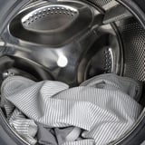 Striped bedsheet inside metal drum washer, highlighting RAMNEFJÄLLs machine washable feature.