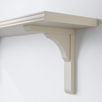 Light beige shelf bracket mounted on white wall, holding empty shelf. Reversible design suits 20 or 30 cm deep shelves.