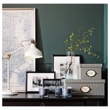 Black desk with vintage lamp, nyc map, photos, vases, and storage boxes.