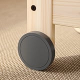 Dark grey, round floor lock on wooden furniture leg, carpeted floor.