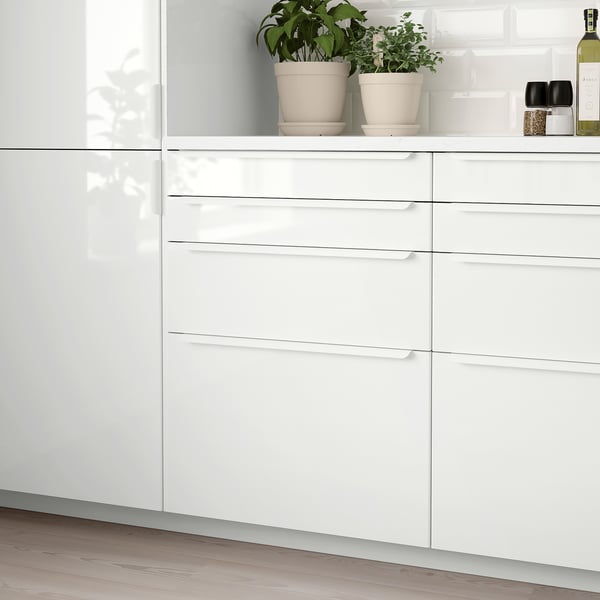 Modern white kitchen corner with glossy RINGHULT drawers; sleek, clean design; plants & bottle on countertop.