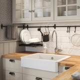 Kitchen sink, wood & white. Black cleaner holder. Dish rack. Glass cabinets show dishes.