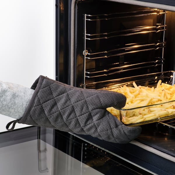 Person wearing gray RINNIG gloves placing tray of food into oven. Gloves protect hands from heat.
