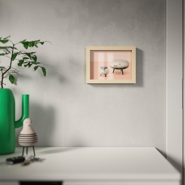 Frame on wall with picture of stools. Green vase with plant on table below. Modern, versatile decor piece.