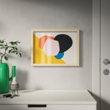 Framed modern art print hangs on wall next to plant and door, showcasing abstract shapes.