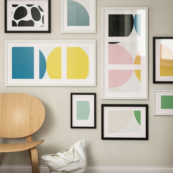 Colorful gallery wall with abstract art. Blue-yellow piece central. Wooden chair with cushion.