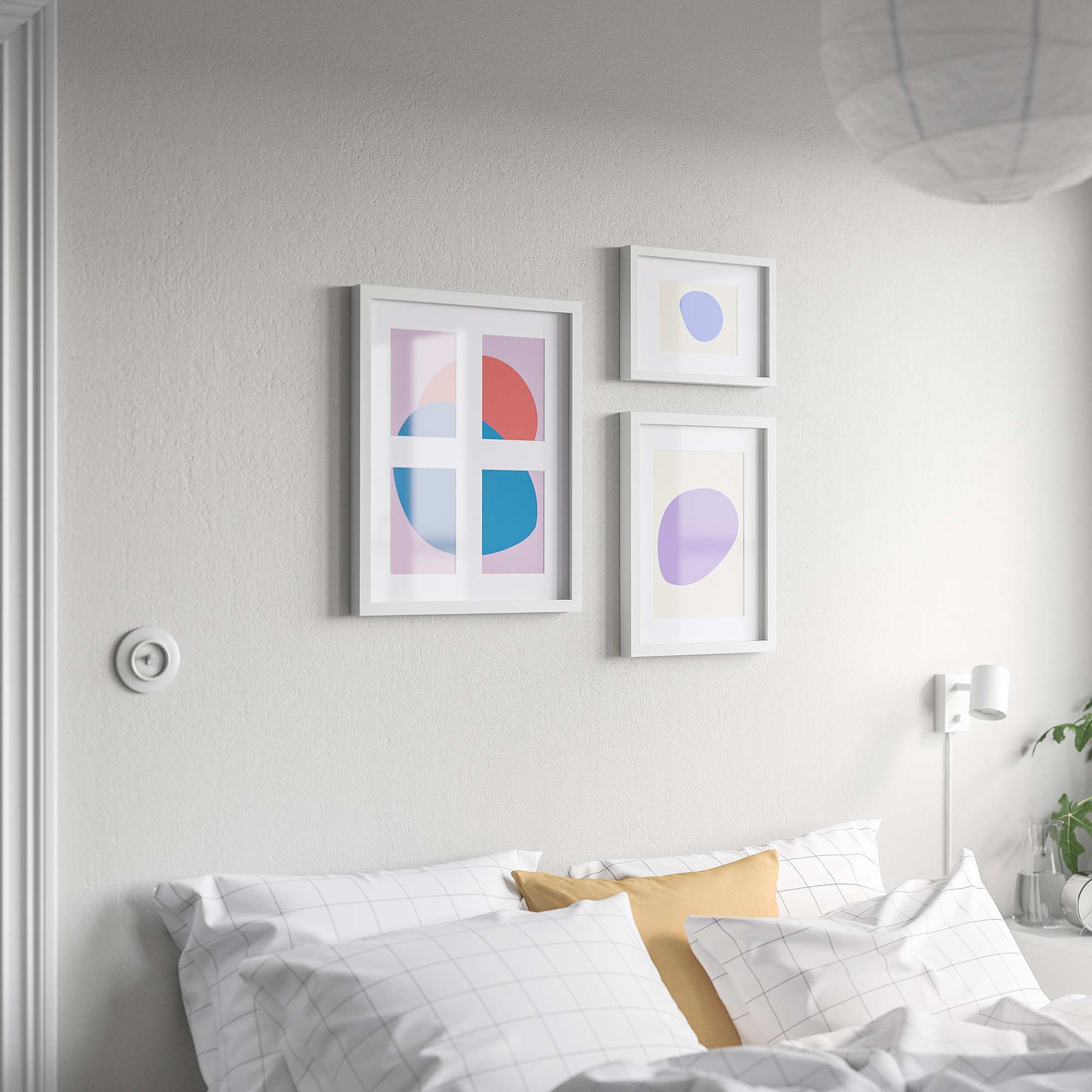 Three RÖDALM frames above bed: left with shapes, others single blobs. White frames, largest left. Bed has grid pillows and yellow bolster.