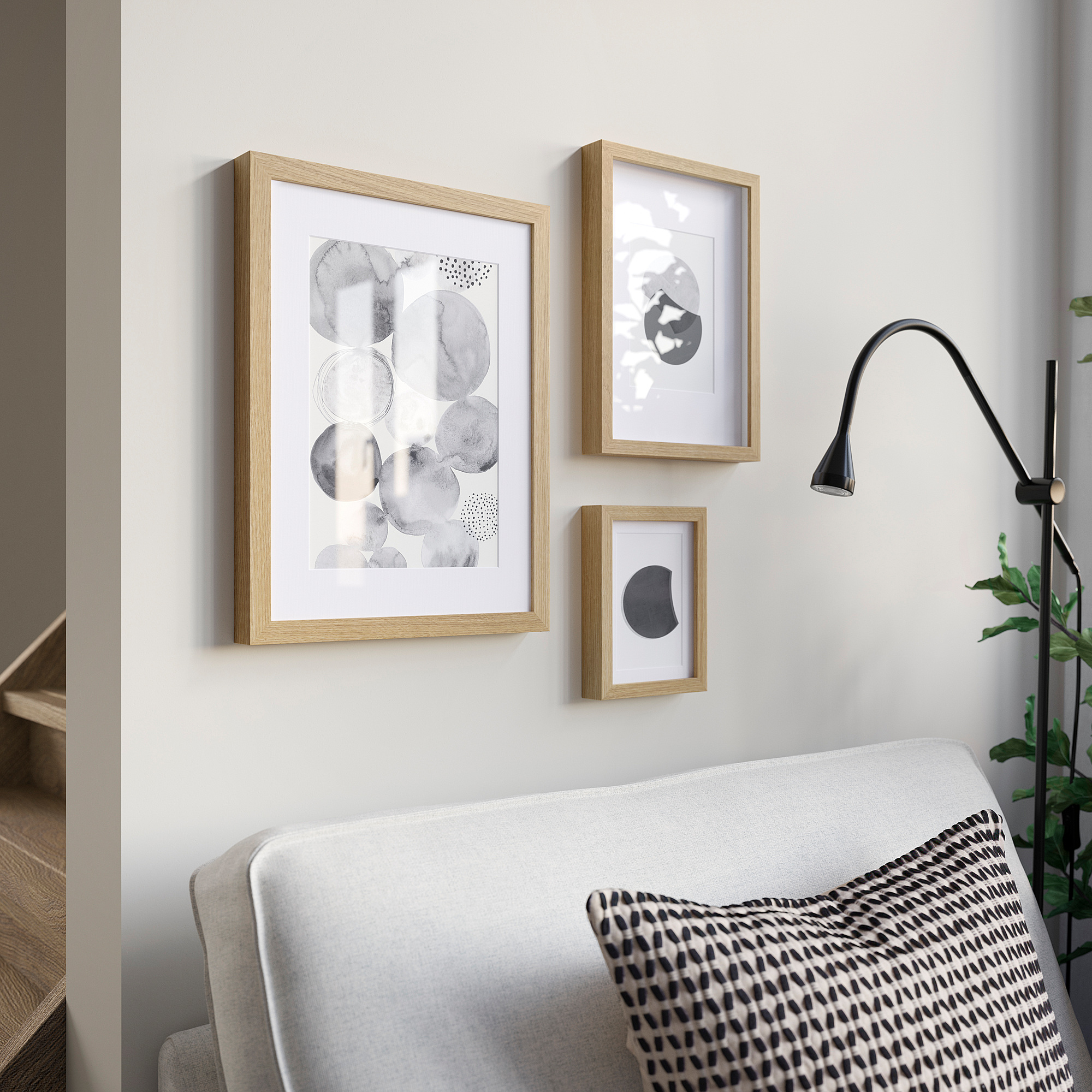 Modern living room with light wood picture frames, abstract prints, grey sofa, and black lamp.