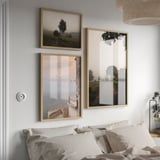 Three light wooden frames above bed show landscapes. Largest on right, smaller ones left. White & gray bedding, wicker pendant lamp above.