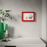 Red-framed picture on gray wall, with modern decor and green vase.