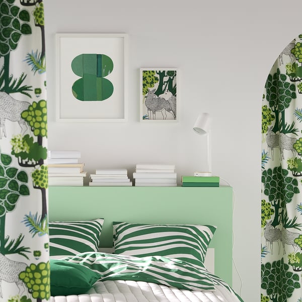 Bedroom with green bedding and wall art. RÖDALM picture frames above bed, smaller than walls.