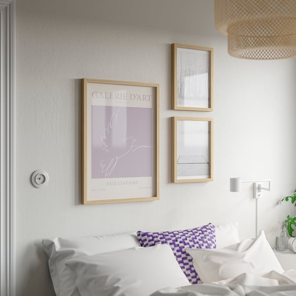Bedroom with white walls, bed, and three framed posters; largest poster reads galerie dart.