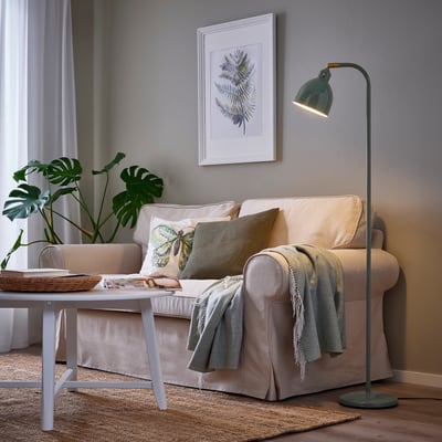 Cozy living room with RÖDFLIK lamp lighting a beige sofa, coffee table, and leaf art.