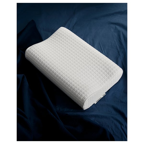 White ergonomic pillow on dark blue bedding, diamond-patterned design.