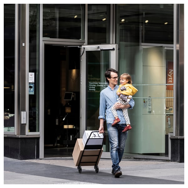 Man exits store with child and box in gray trolley.