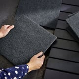 Assembling black RUNNEN floor tiles on dark wood balcony.