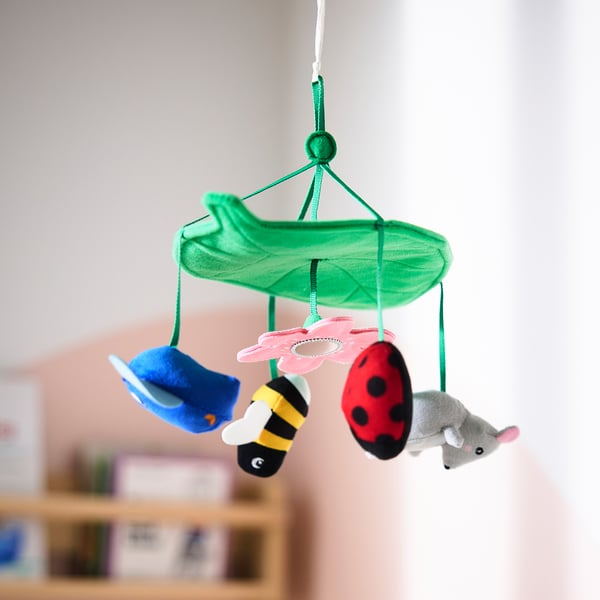 Colorful baby mobile with owl, ladybug, bee, and mouse suspended from a green leaf, designed to stimulate vision and curiosity.