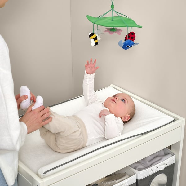 Baby reaches for colorful mobile above changing table, which stimulates vision and curiosity.