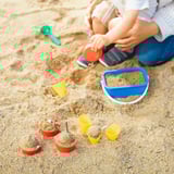 Child playing with SANDIG sand toys, including cups and a scoop, developing motor skills on the sand.