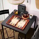 Modern black counter-height dining table with red backgammon set and tea.