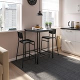 Modern kitchen with small black sandberg bar table and stools. White walls, big windows, and city view.