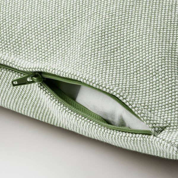 Close-up of a green zipper on a woven cushion. The zipper is partially open, revealing the cushions white liner.