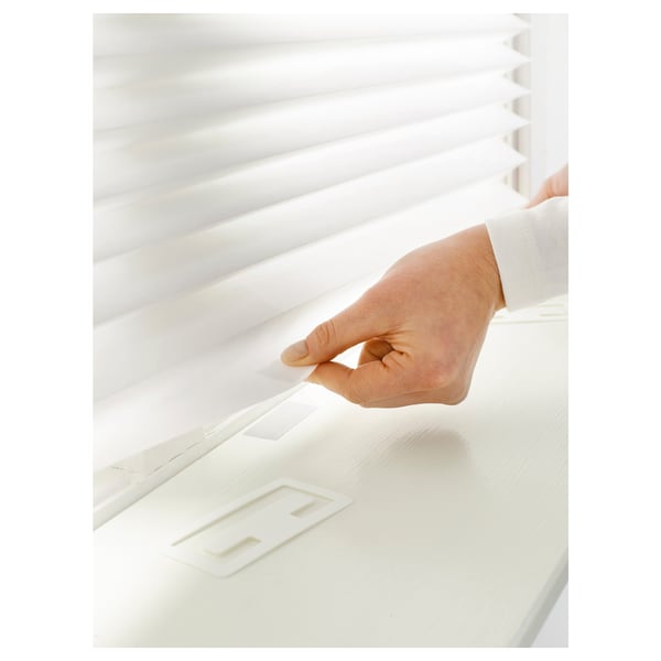 Person attaching white pleated blind to window, securing with clip for privacy and light control.