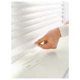 Person attaching white pleated blind to window, securing with clip for privacy and light control.