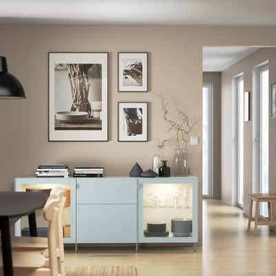 Modern dining space with blue sideboard, art, plates, vases, black table, wooden chairs.