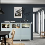 Grey-blue cabinet displays dishes in modern living room with dark grey wall and decor.