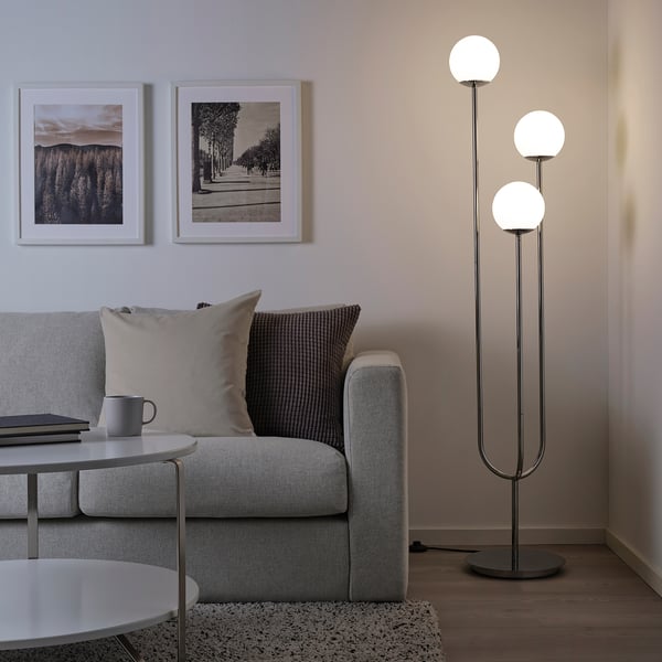 Modern living room with grey sofa, coffee table, framed photos, and tall chrome floor lamp with glass globes illuminating the space.