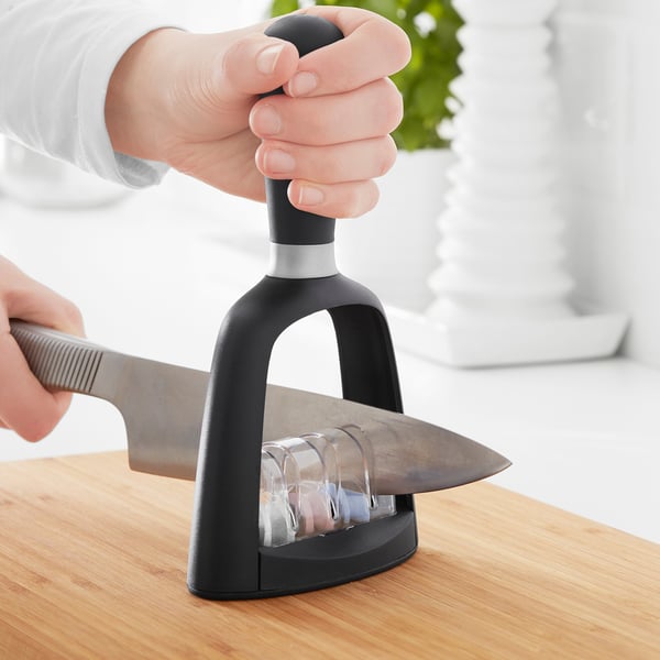 Person sharpening knife using electric sharpener on wooden table.