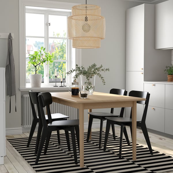 SKANSNÄS dining set with extendable table, 4 black chairs, & butterfly leaf. Decor includes plant, candles, & vase. Bright room with window & rug.
