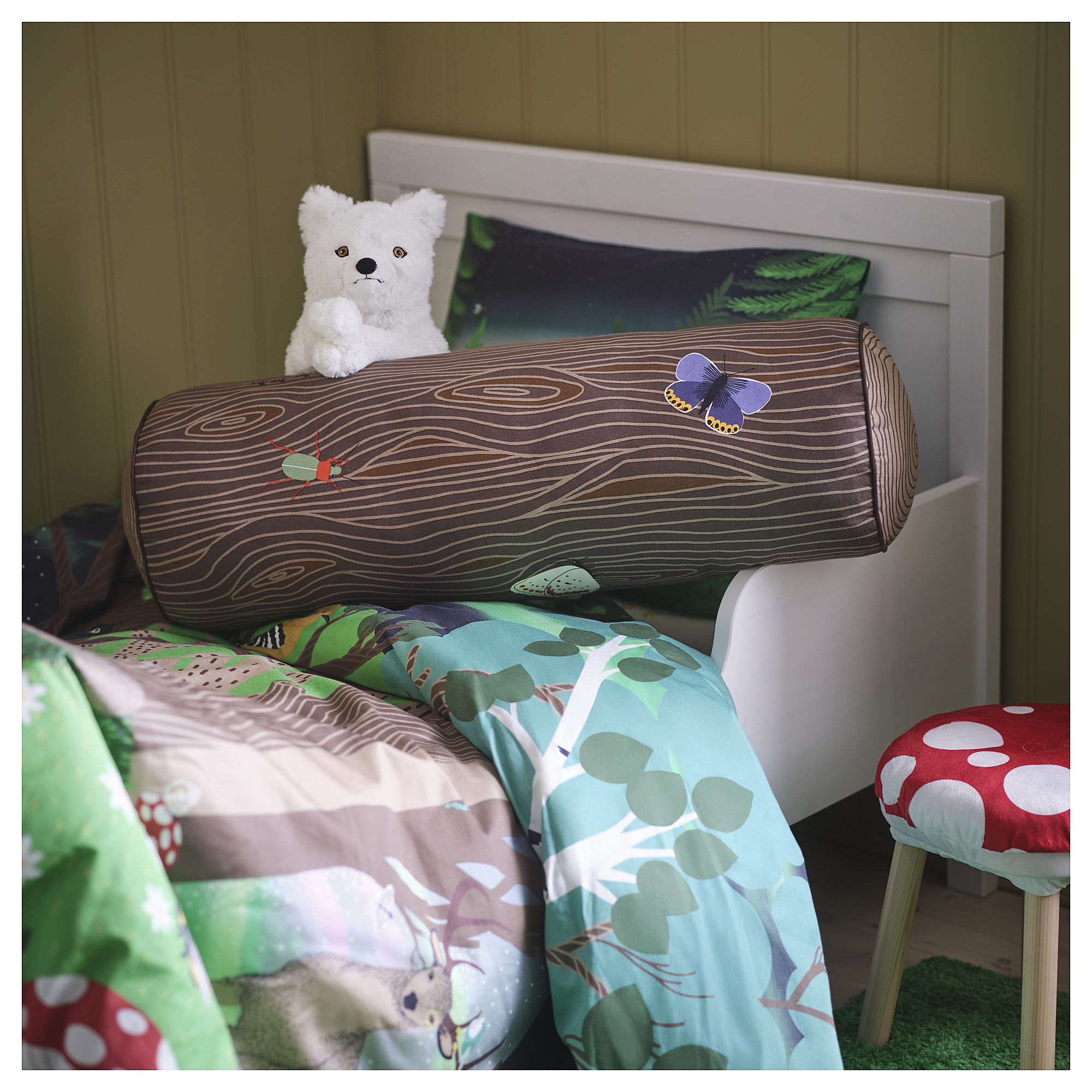 SKOGSDUVA: tree trunk-shaped pillow with insects on bed, white wall.