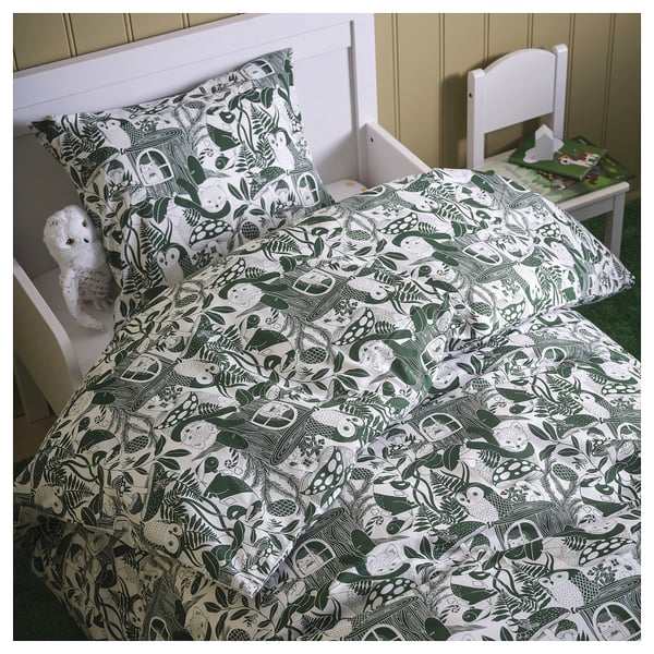 Cozy bed with woodland-themed duvet, teddy bear, and small chair with books and toys.