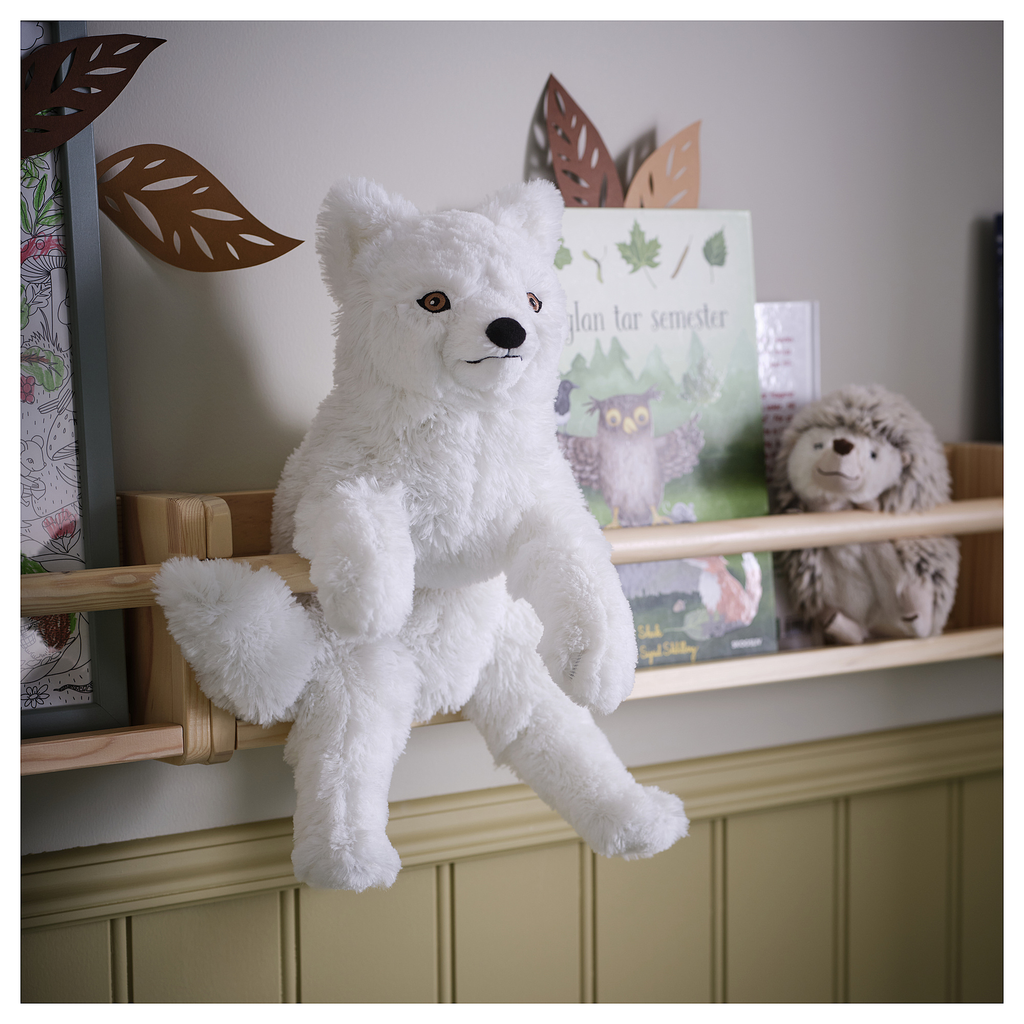 White SKOGSDUVA fox on shelf. Next to gray hedgehog & green book. Soft, fluffy, with safe materials.