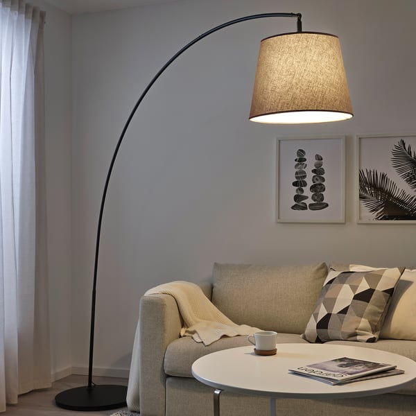A living room with a beige fabric SKOTTORP lamp arched over a small round table before a couch.