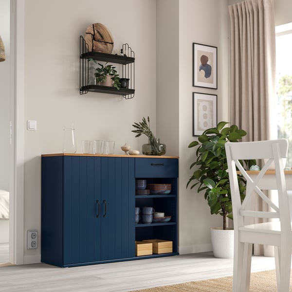 Modern dining room with blue SKRUVBY sideboard and open shelves, complemented by a white chair and large green plant, with wall art and curtains.