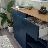 Blue sideboard with drawer open, displaying cutlery and napkins on wooden top beside potted plant.