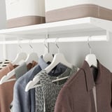 Closet with hangers and shelves. Clothes hung neatly on white hangers, with storage containers above, maximizing space and visibility.