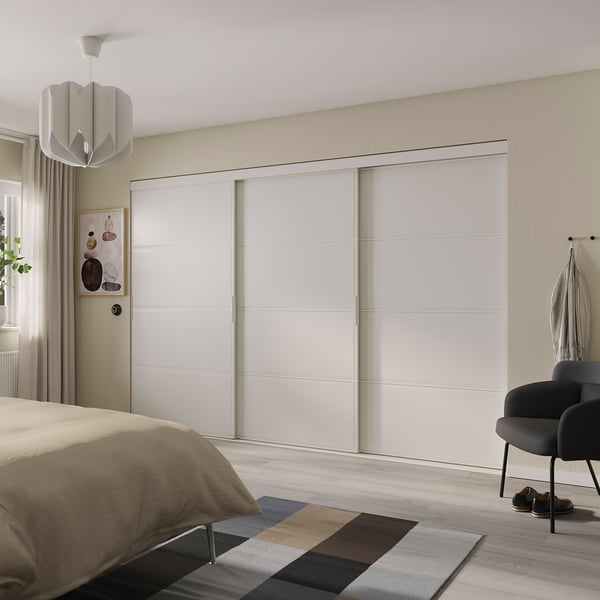 Bedroom with large white SKYTTA sliding closet doors, modern decor, beige bedding, colorful rug, and black chair.