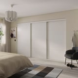 Bedroom with large white SKYTTA sliding closet doors, modern decor, beige bedding, colorful rug, and black chair.